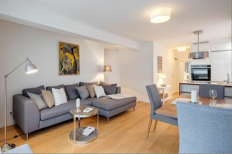 Bestlage Modern eingerichtetes Wohnzimmer mit offener Küche und gemütlichem Essbereich – stilvoll möblierte Wohnung zur Miete oder zum Kauf bei Mr. Lodge in München.